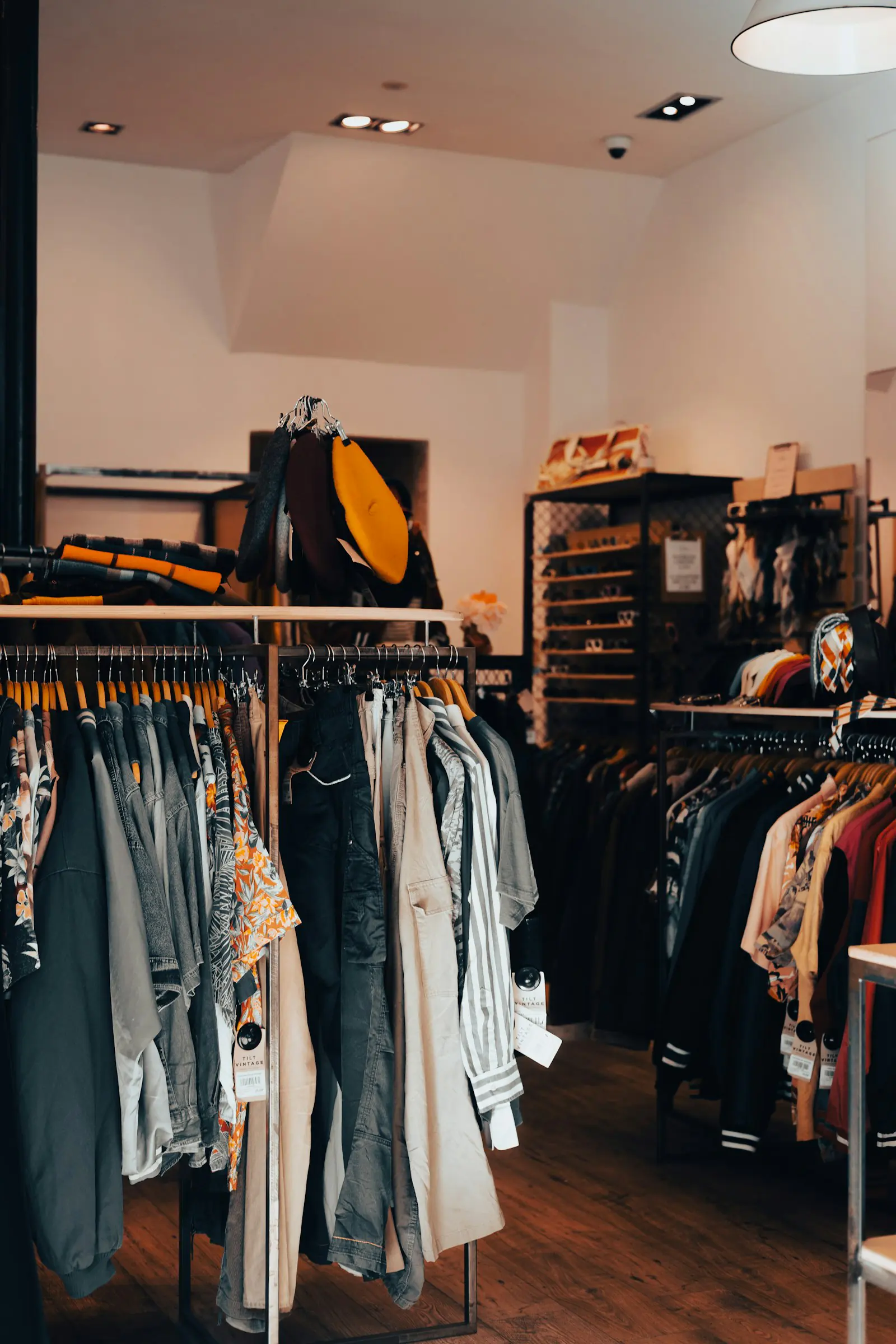 Clothing racks in a shop with wooden floors, including patterned shirts, trousers, and jackets, photographed in Bordeaux.