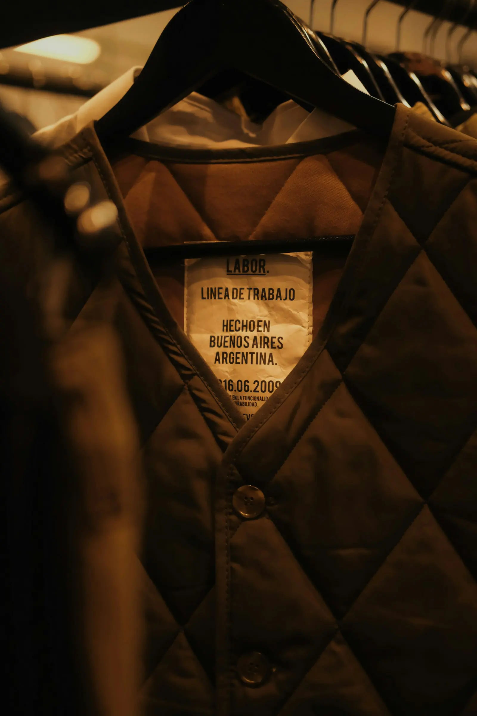 Close-up of an olive quilted vest on a hanger, with a white inner label reading LABOR and Hecho en Buenos Aires.